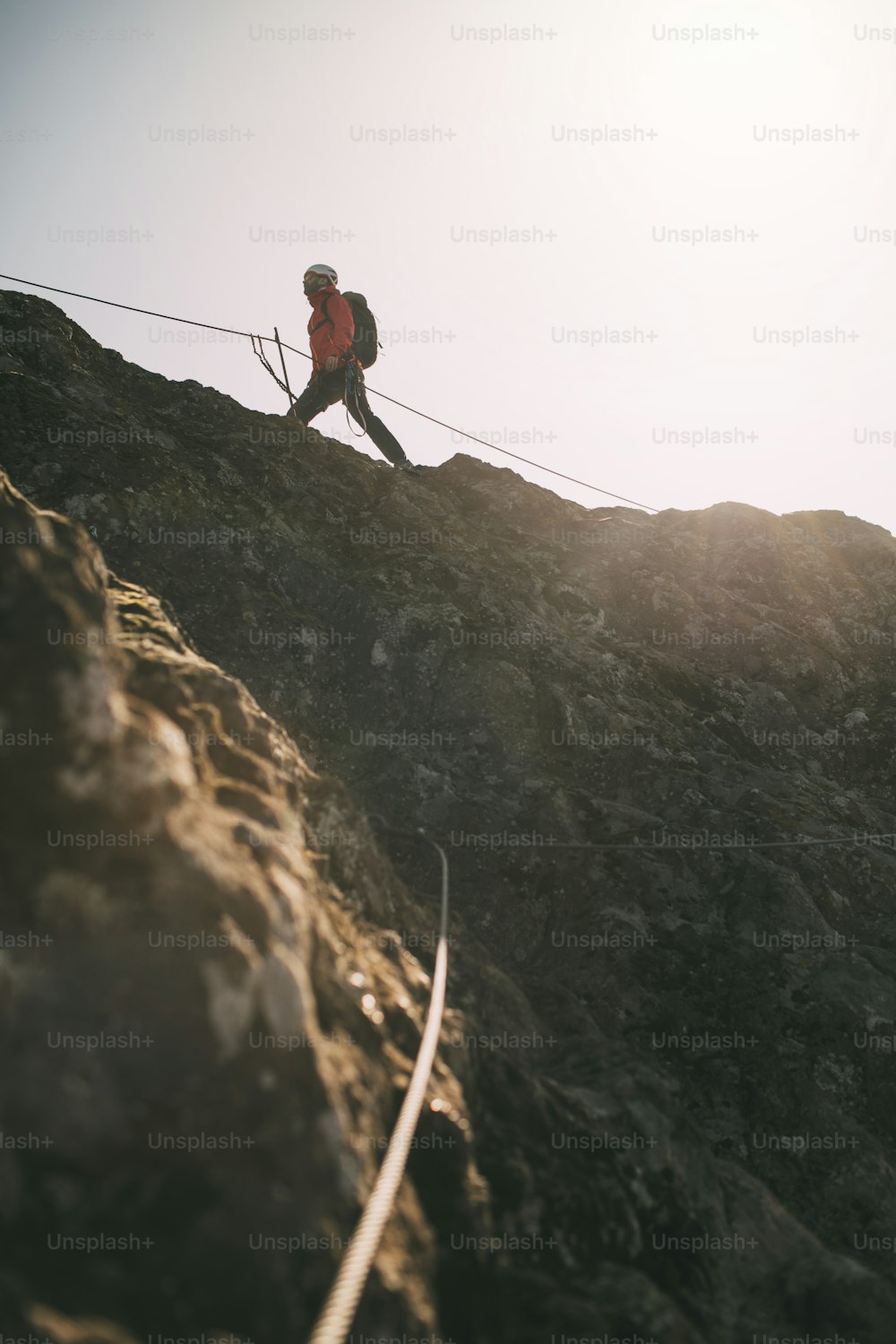 岩山の頂上を登るために登山ロープを使用してバックパックを背負った登山家。