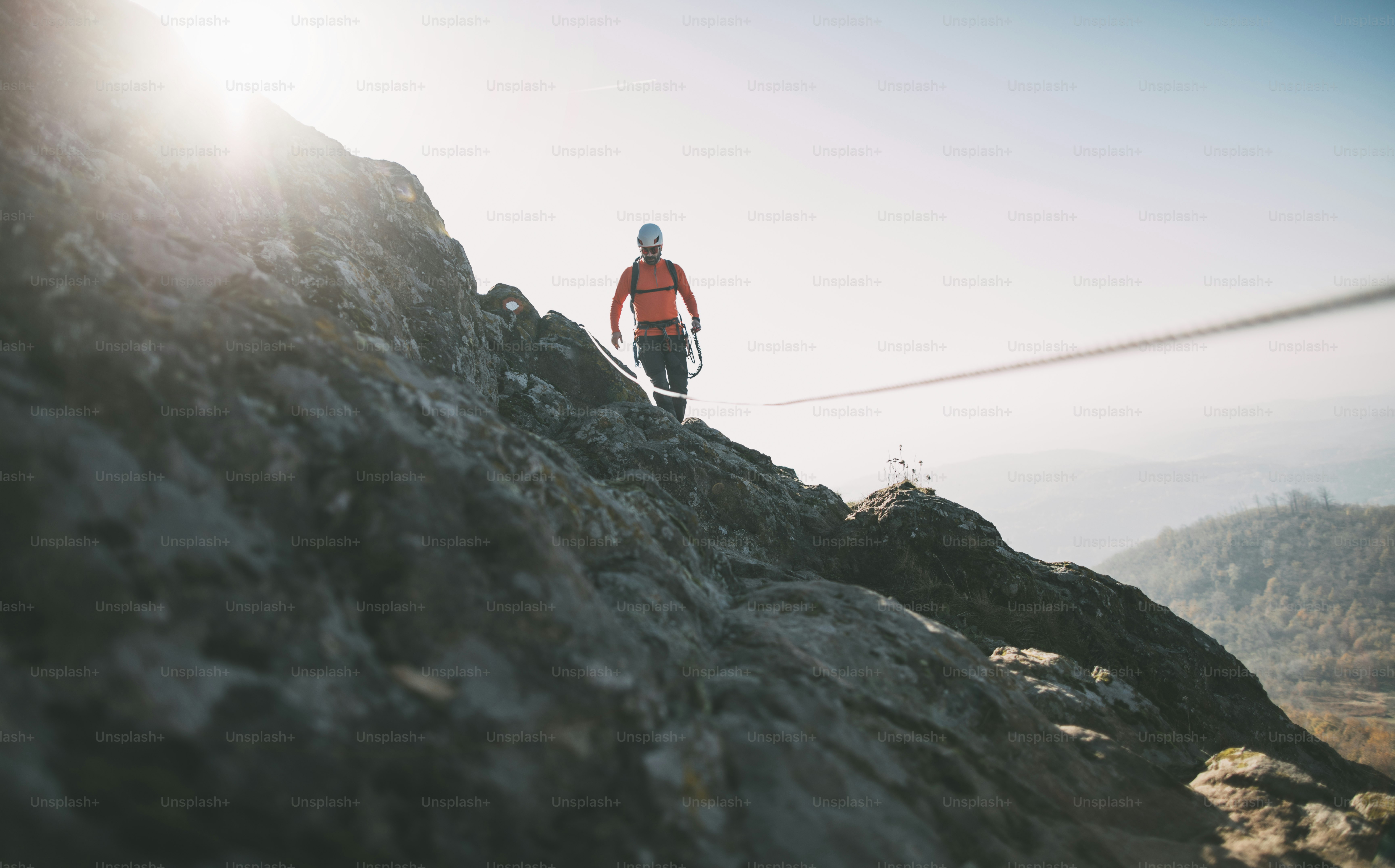 Mountaineer with backpack using climbing rope to climb rocky mountain summit. photo Adventure