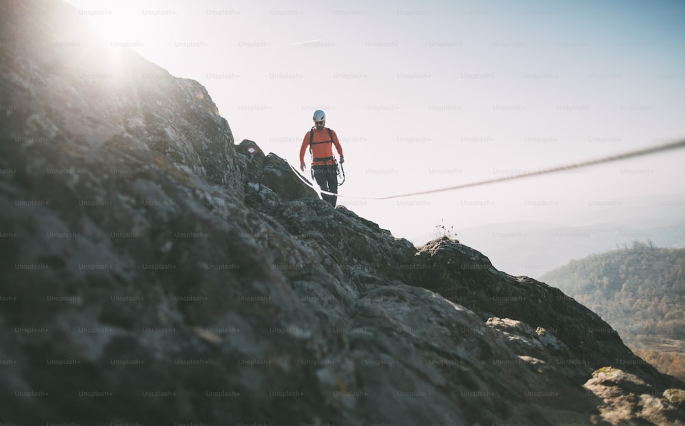 Mountaineer with backpack using climbing rope to climb rocky mountain summit.