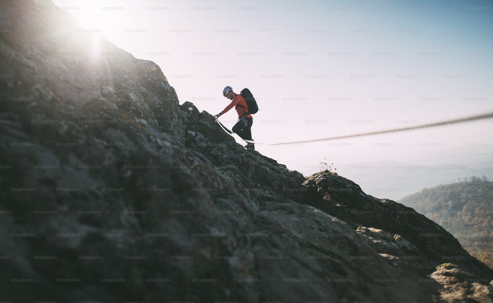 Alpinista con zaino che utilizza la corda da arrampicata per scalare la cima rocciosa della montagna.