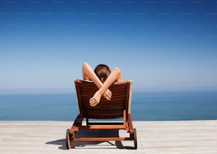 a woman laying on top of a wooden chair next to the ocean