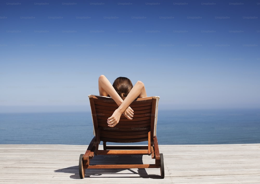 uma mulher deitada em cima de uma cadeira de madeira ao lado do oceano