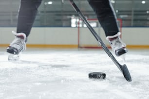 Pernas do jogador de hóquei masculino em uniforme esportivo e patins se movendo para baixo pista na frente da câmera contra o ambiente do estádio enquanto vai atirar puck