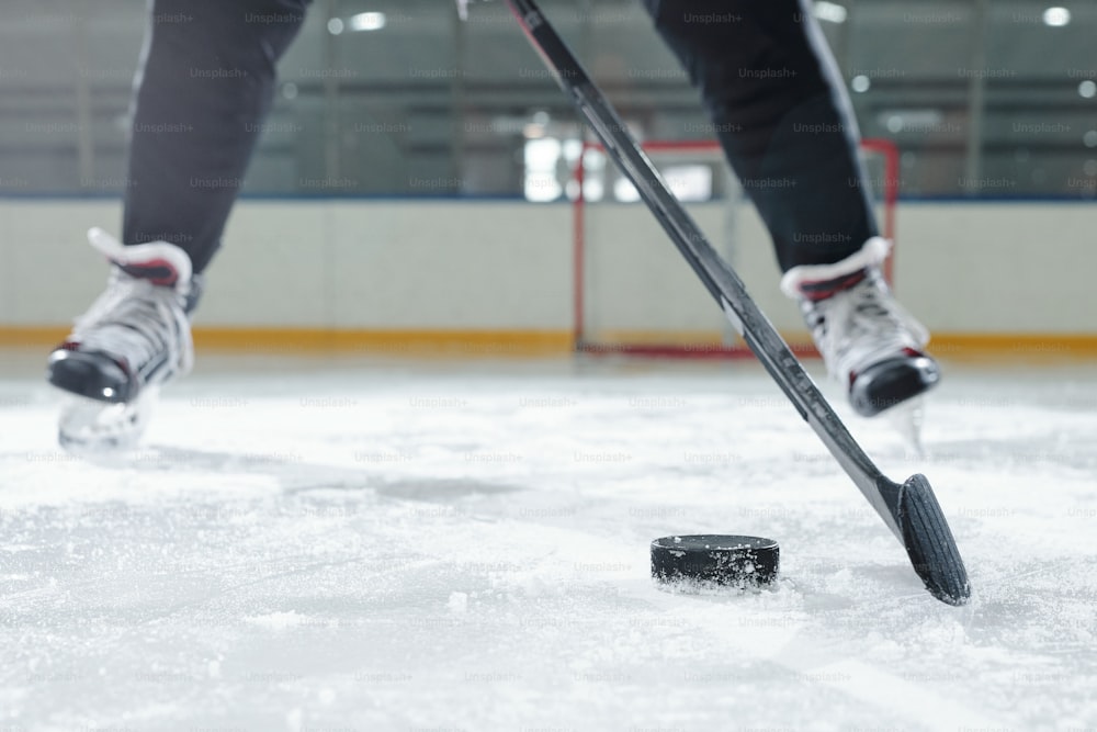 Gambe del giocatore di hockey maschio in uniforme sportiva e pattini che si muovono lungo la pista davanti alla telecamera contro l'ambiente dello stadio mentre vanno a sparare il disco