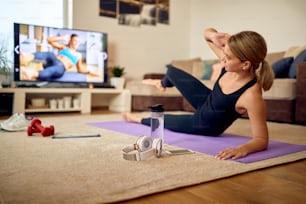 Athletic woman practicing side sit-ups in front of a TV in the living room.