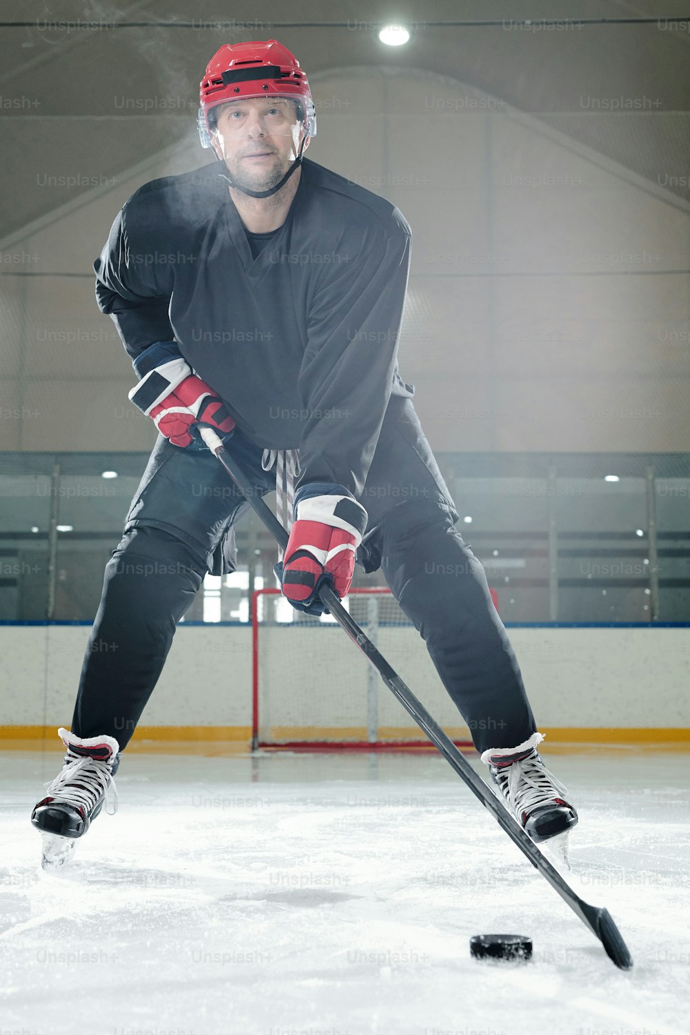 Mature male hockey player in sports uniform, protective helmet and gloves moving down rink in front of camera and going to shoot puck