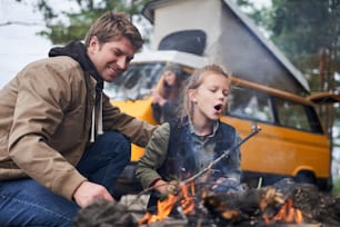Incredible adventure. Little cute daughter blowing on a burning stick by the fire. Father rejoices of his little helper
