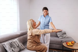 Senior woman sitting on couch with stretched arm while nurse checking on her arm.