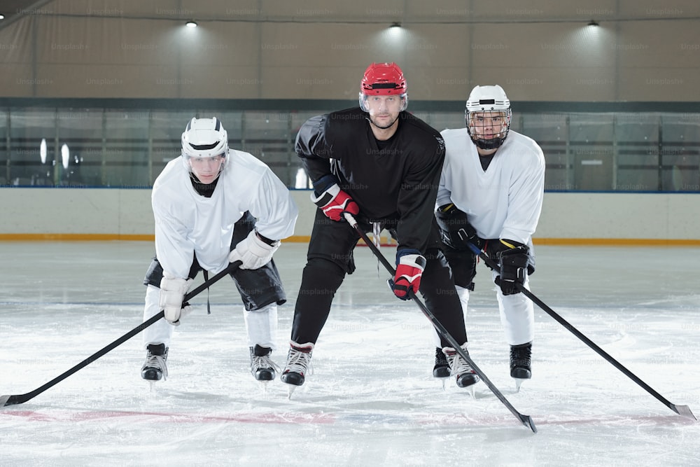 Tres jugadores profesionales de hockey con uniforme, guantes, patines y cascos se inclinan hacia adelante mientras están de pie en la pista de hielo durante el entrenamiento antes del juego