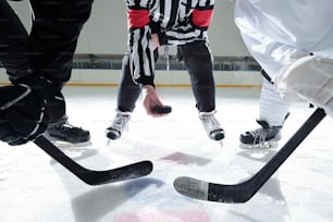 Hockeyschiedsrichter mit Puck auf Eisbahn stehend mit zwei Rivalen mit Stöcken rechts und links und wartet auf einen Moment, um ihn zu schießen