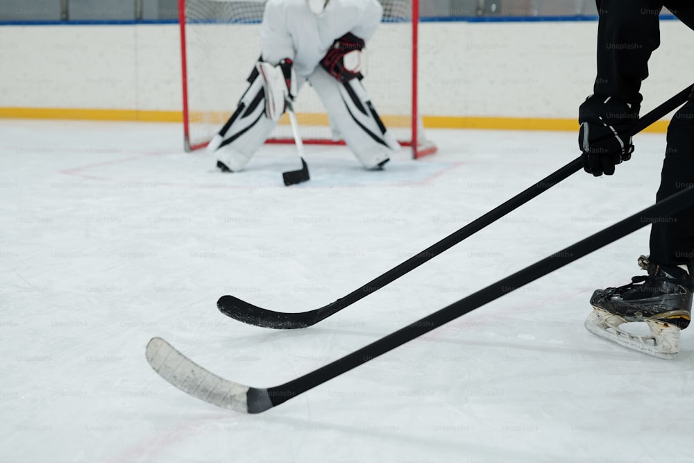 Palos de hockey sostenidos por dos jugadores en patines, guantes y uniforme deportivo en el fondo del portero que se prepara para atrapar el disco