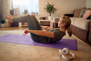 Athletische Frau mit Handgewichten beim Sit-up im Wohnzimmer.