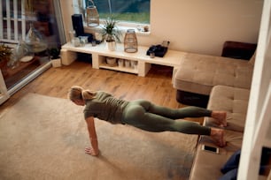 High angle view of sportswoman doing push-ups while holding her legs on the sofa during home workout.