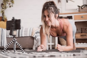 집에서 운동하는 젊은 스포티 한 여성, 전화로 온라인 개인 훈련 프로그램을 사용하여 엉덩이 몸 형성을 위해 거실 바닥에서 피트니스 운동을하는 십대, 실내에서 요가 필라테스