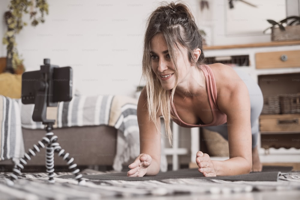 Junge sportliche Frau, die zu Hause trainiert, Teenager macht Fitnessübungen auf dem Wohnzimmerboden für Gesäß Körperformung mit Online-Personal Training-Programm mit Telefon, Yoga Pilates drinnen