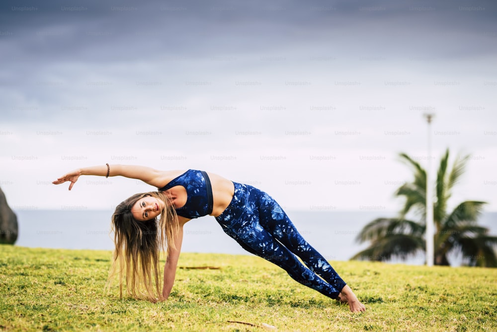 Schöne junge erwachsene Frau in ausgewogener Pilates-Übungsposition im Freien - Sport aktive Menschen und gesunder Lebensstil Konzept - fröhliche kaukasische Frau machen Yoga
