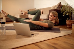 Happy female athlete using laptop while exercising on the floor in the living room.