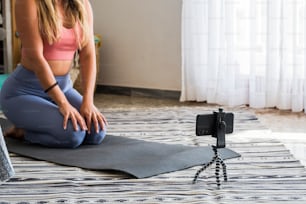 Foto de una mujer fitness sentada en una colchoneta de yoga y usando un teléfono móvil. Mujer joven en forma usando el teléfono celular mientras hace ejercicio en casa. creador de contenido gente de negocios moderna en línea internet