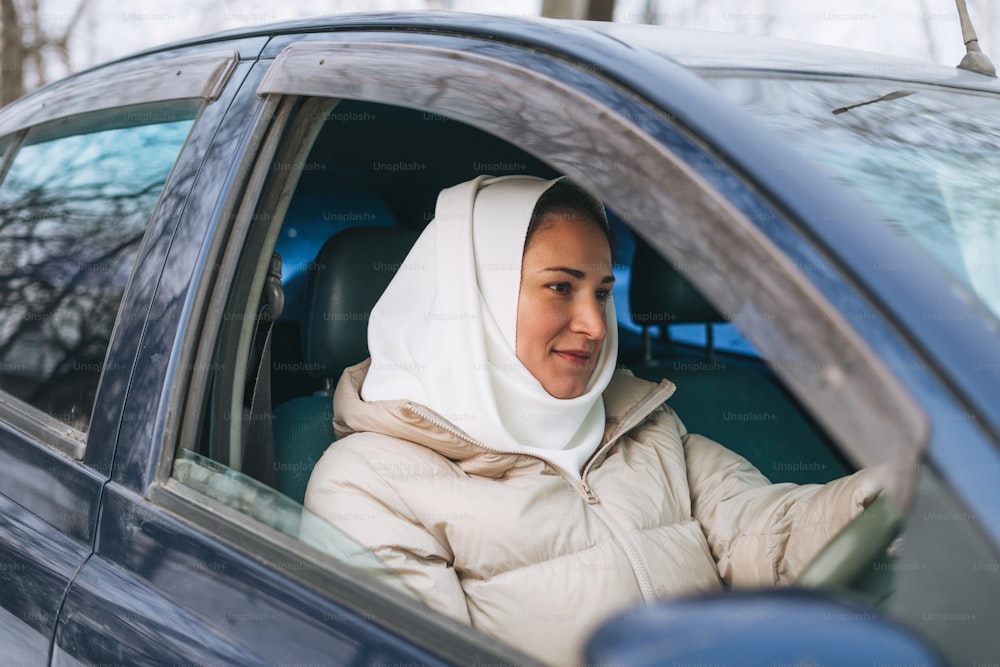 Hermosa mujer musulmana joven sonriente en pañuelo en ropa ligera en coche con volante a la derecha