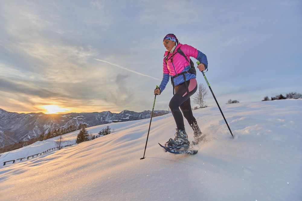 Paesaggio al tramonto in montagna con ragazza che corre in discesa con le racchette da neve
