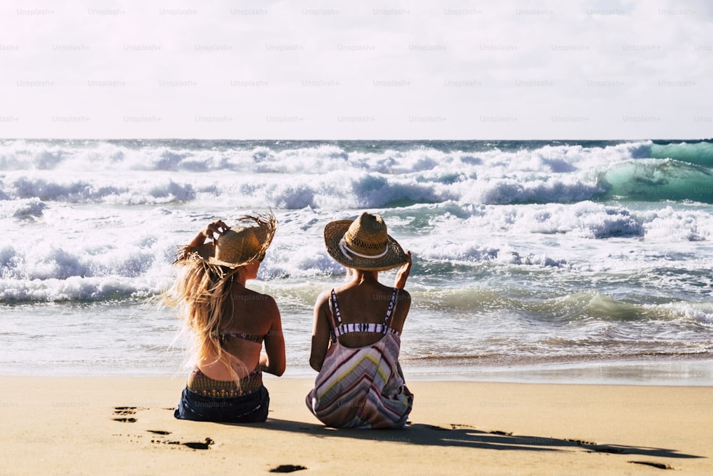 Pareja de amigas de mujeres en el viaje vacaciones de verano se relajan y disfrutan del ocio al aire libre en la playa sentados en la arena y mirando el agua azul del océano y el cielo - concepto de jóvenes gratis