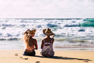 Couple of women friends in travel summer holiday vacation relax and enjoy the outdoor leisure at the beach sitting on the sand and looking blue ocean water and sky - concept young people free