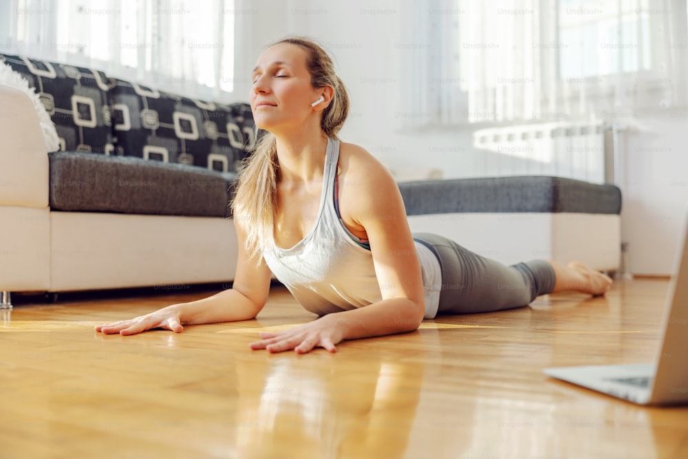 Mujer yogui tranquila en postura de yoga cobra después de una conferencia en línea en casa.
