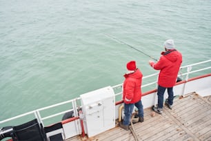 Vue en grand angle du jeune marin aidant le pêcheur diligent à sortir d’énormes poissons de la mer ou de l’océan pendant la pêche à la journée d’hiver. Banque d’images
