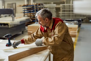 Ouvrier marquant les mesures sur une pièce de bois dans un atelier de menuiserie.