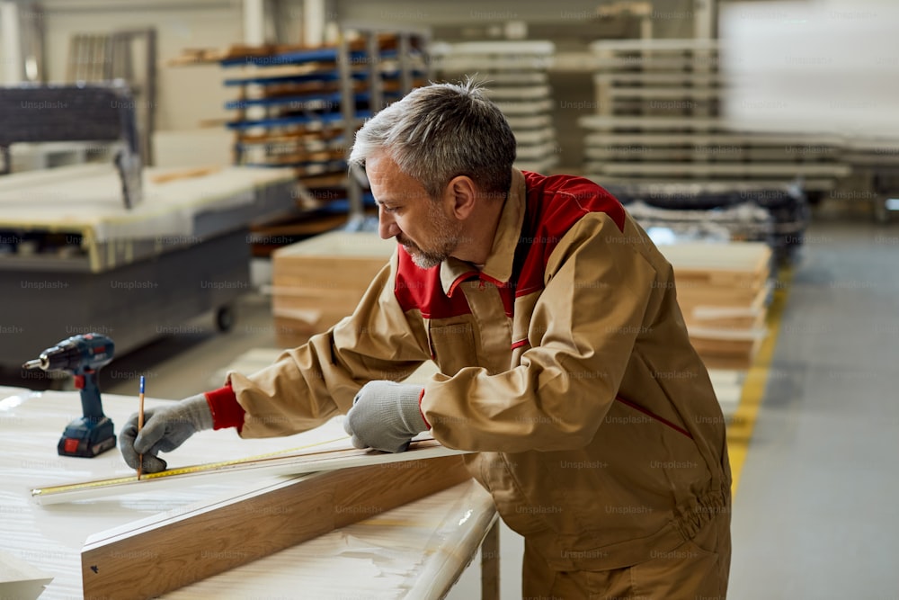 Trabalhador manual marcando medidas em um pedaço de madeira na oficina de carpintaria.