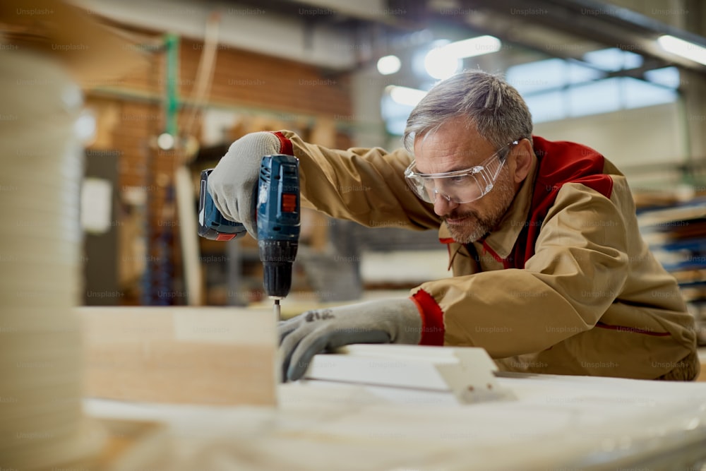 Carpinteiro adulto médio usando uma broca enquanto trabalha com madeira em uma oficina.
