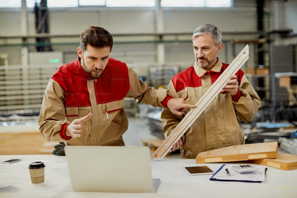 Dos carpinteros usando una computadora portátil y cooperando mientras trabajan en un taller.