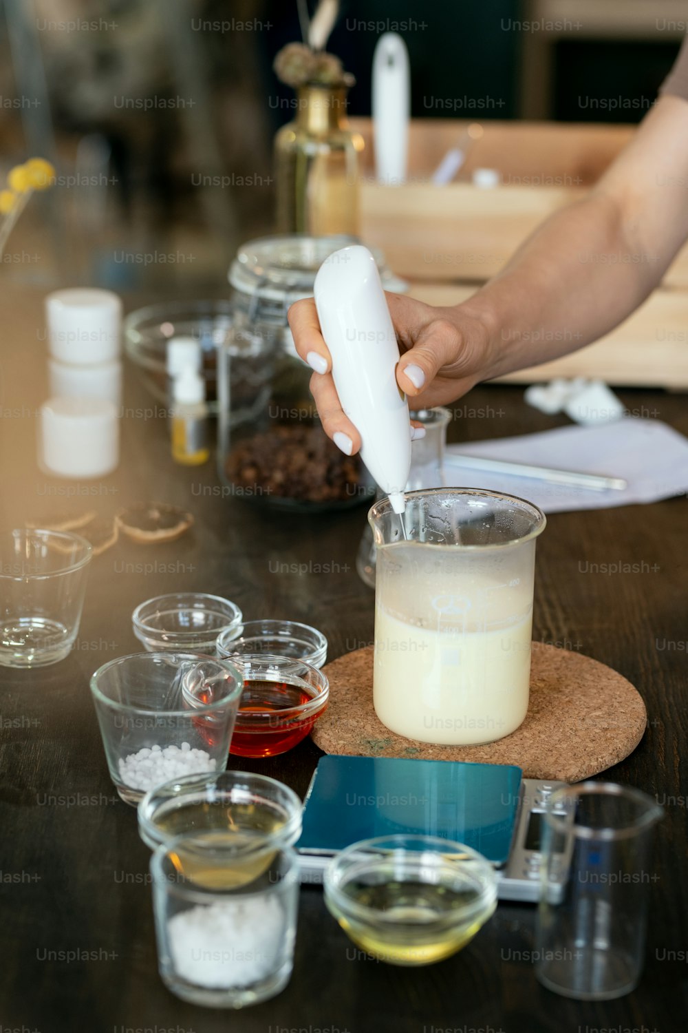 Hand of female putting transparent liquid substance into glassware with melted soap mass while making mixture for handmade cosmetics