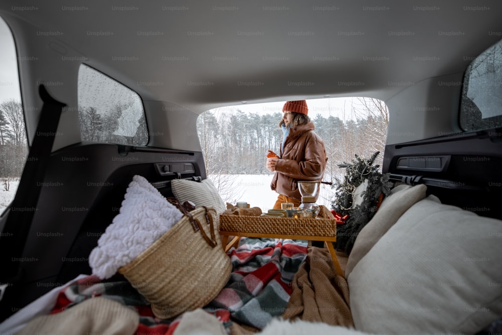 Donna bere caffè vicino al bagagliaio di un'auto, viaggiando con un'auto a noleggio durante le vacanze invernali. Vista dall'interno dell'auto. Foto di alta qualità