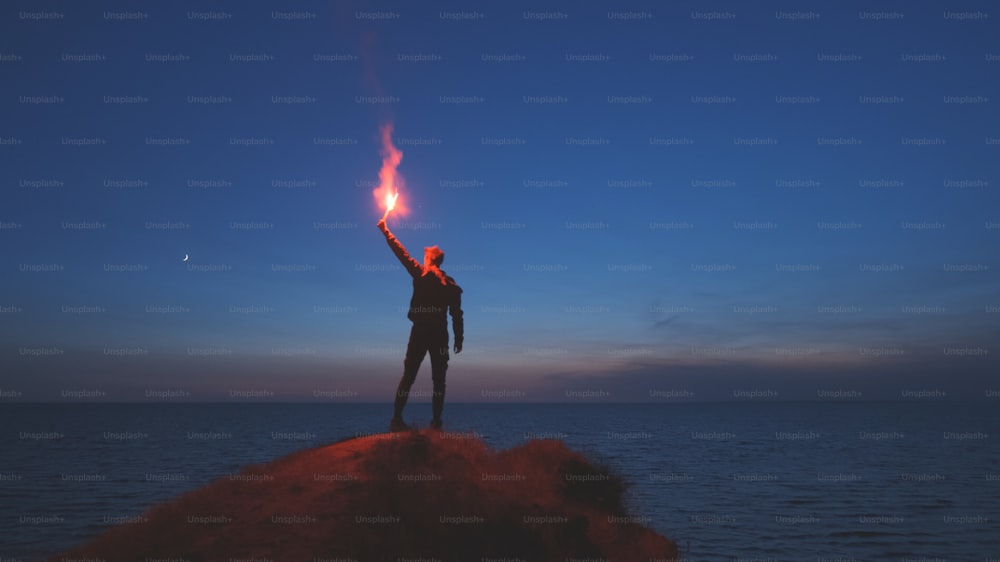 Der Mann mit einem Feuerstab steht auf dem Berggipfel in der Nähe des Meeres
