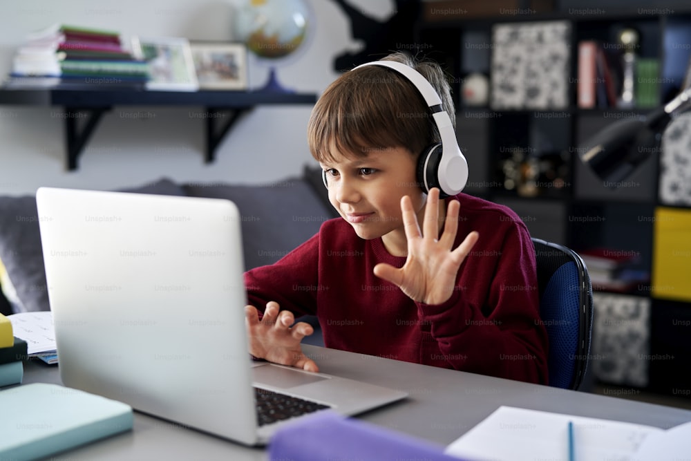 Menino usando laptop e acenando durante a chamada de vídeo enquanto lição de casa