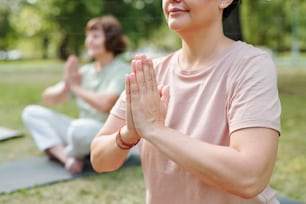 Close-up of mature woman sitting in lotus positon and doing breathing exercises outdoors