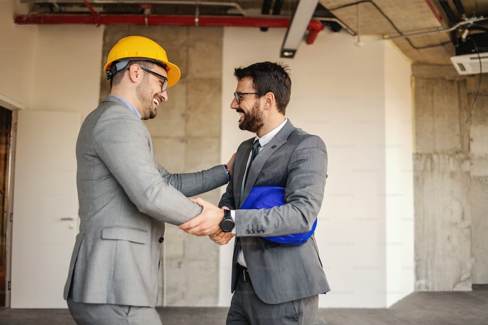 Smiling architect shaking hands with businessman while standing in building in construction process.