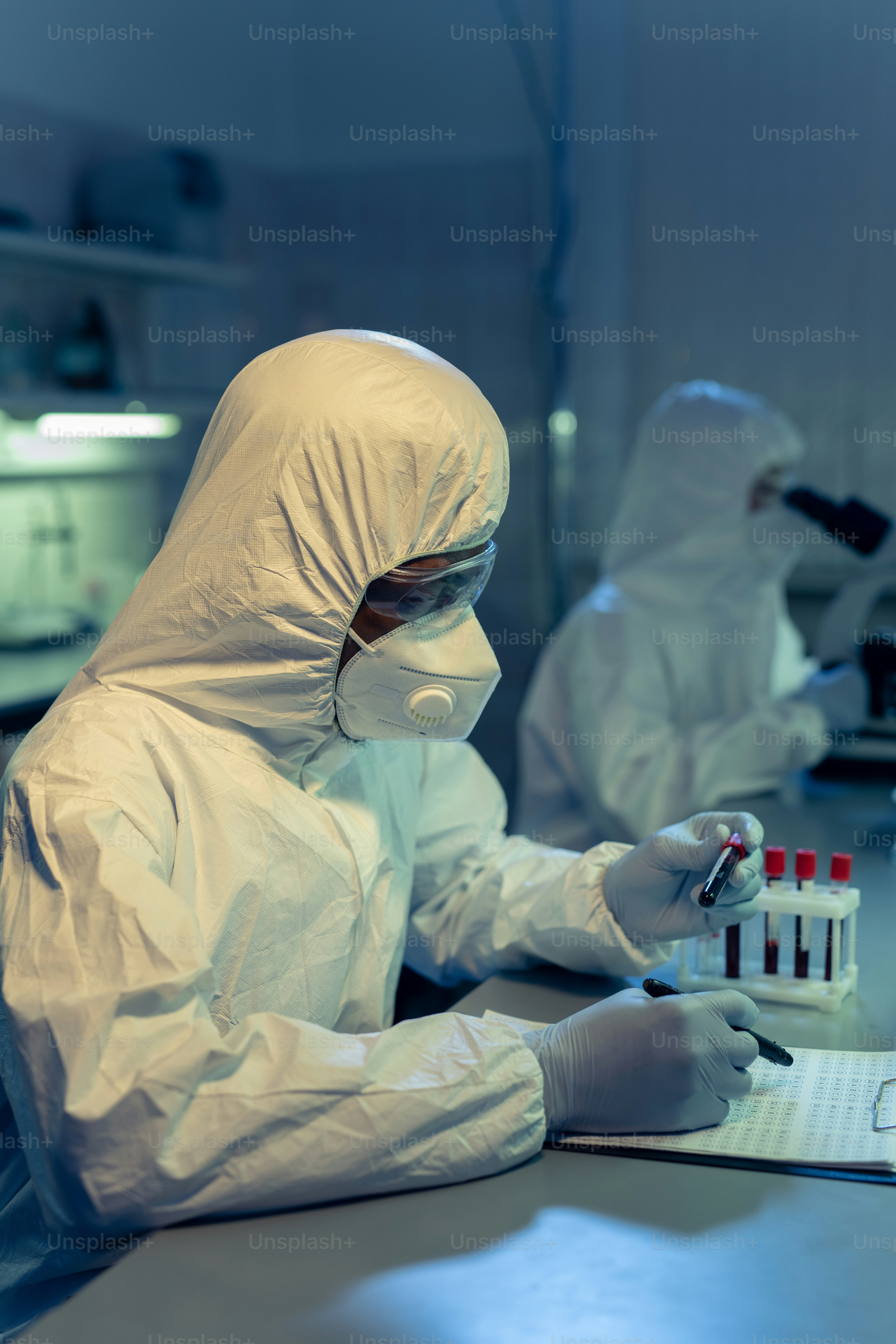 Wissenschaftler in Arbeitsschutzkleidung arbeitet mit seinem Kollegen am Tisch mit gefährlichen chemischen Proben