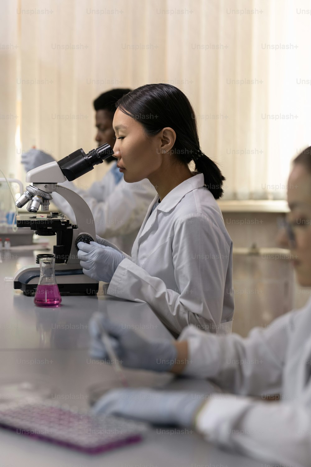 Jovem químico asiático que trabalha com microscópio na mesa enquanto trabalha no laboratório