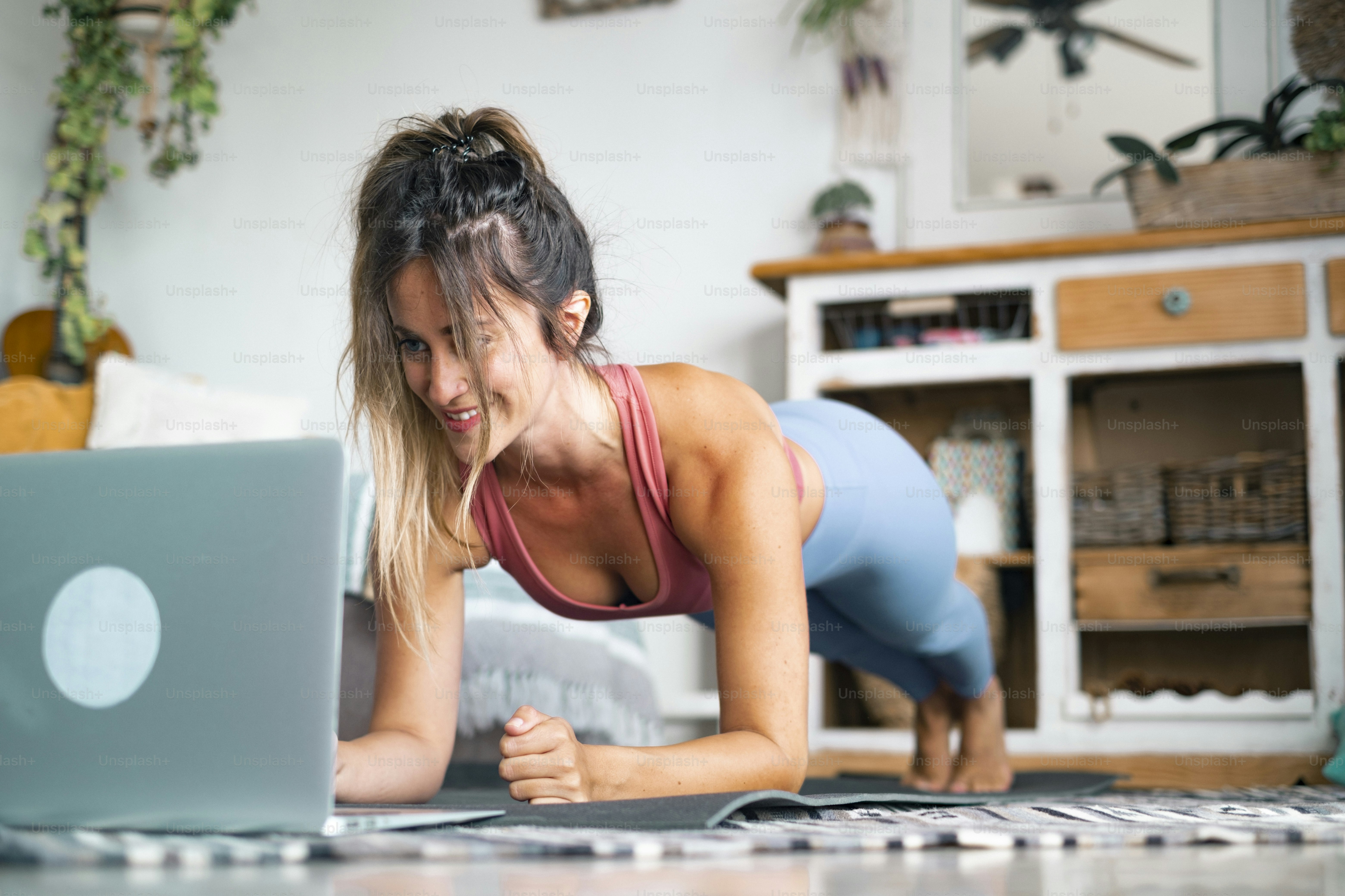 Giovane donna che si esercita a casa facendo flessioni e guardando il suo computer portatile personale per imparare o insegnare l'allenamento - concetto di persone di stile di vita sano gratuito per il creatore di contenuti