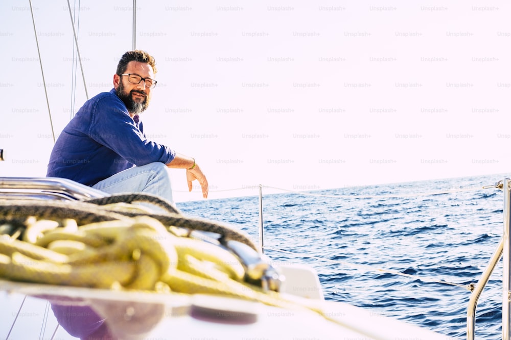 Retrato do homem sentar-se no convés do barco a vela e olhar longe para o oceano - pessoas adultas do sexo masculino gostam de viagens e estilo de vida - imagem do conceito marinho e de navegação - céu brilhante ao fundo - excursão de verão