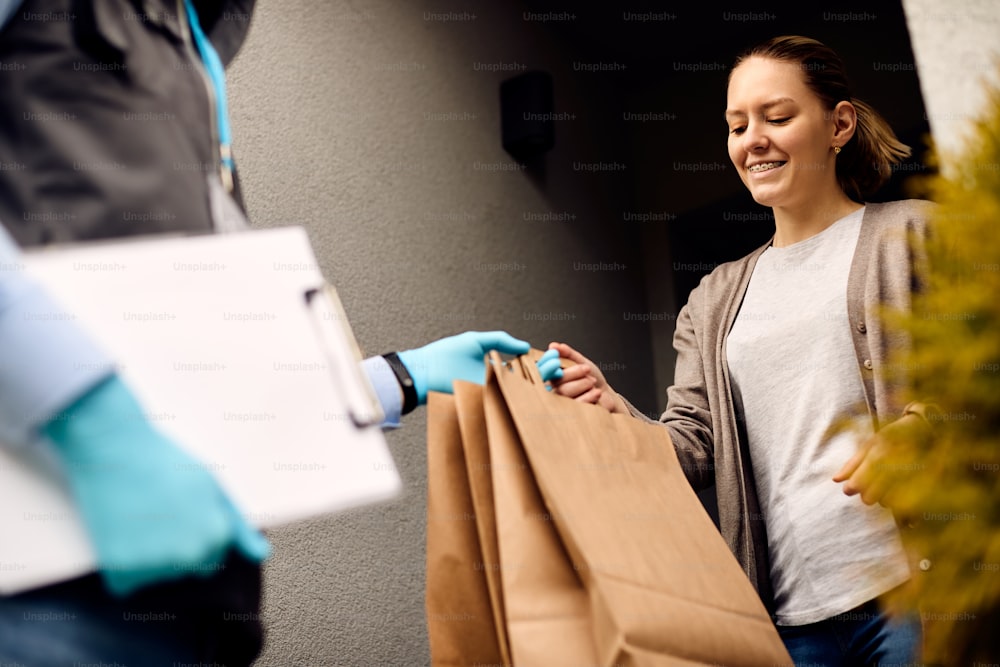 Vista de ángulo bajo de una mujer sonriente que recibe la entrega a domicilio y toma las bolsas del repartidor.