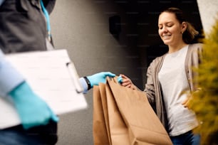Vue en contre-plongée d’une femme souriante recevant une livraison à domicile et prenant des sacs du livreur.
