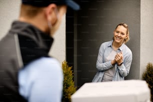 Mujer feliz de pie en la puerta y saludando al repartidor que lleva cajas de pizza.