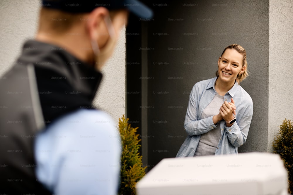 Mulher feliz de pé na porta e cumprimentando o entregador que está carregando caixas de pizza.