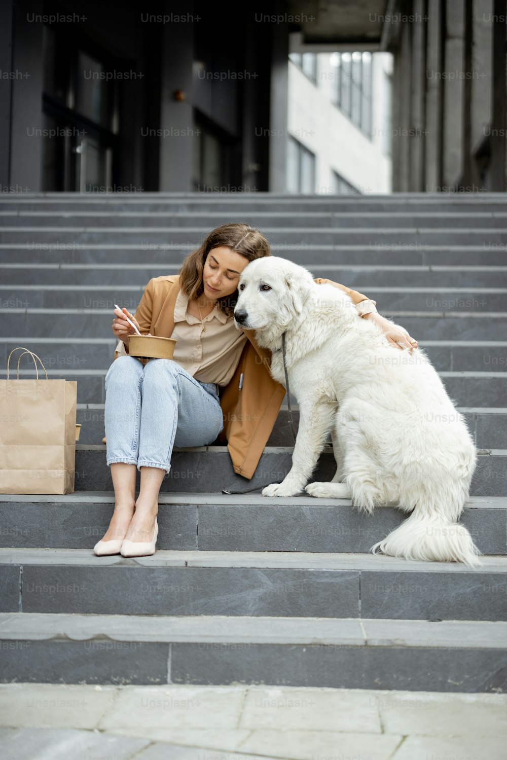 Pretty woman have outdoor lunch near office building with her big white dog while sitting on the stairs, hugs her dog. Pet friendly and pet care concept. Animal lover.