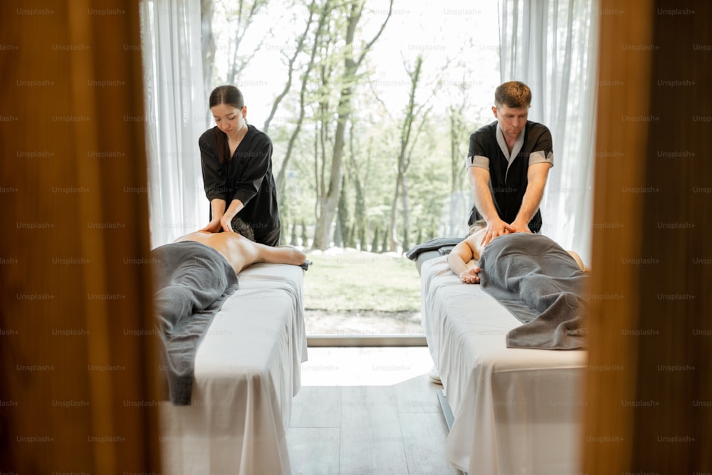 Two masseurs doing a deep back massage to guests with pampering technique. Wellness and leisure time for health care together with forest view in window.
