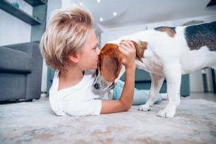 Niño lindo jugando con el perro en el piso de la casa - Niño besando a su amigo mascota acostado en la alfombra - Concepto de niños y perros