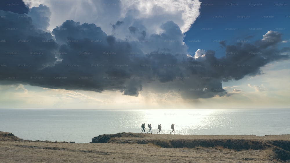 The group of four people walking to the mountain edge near the sea